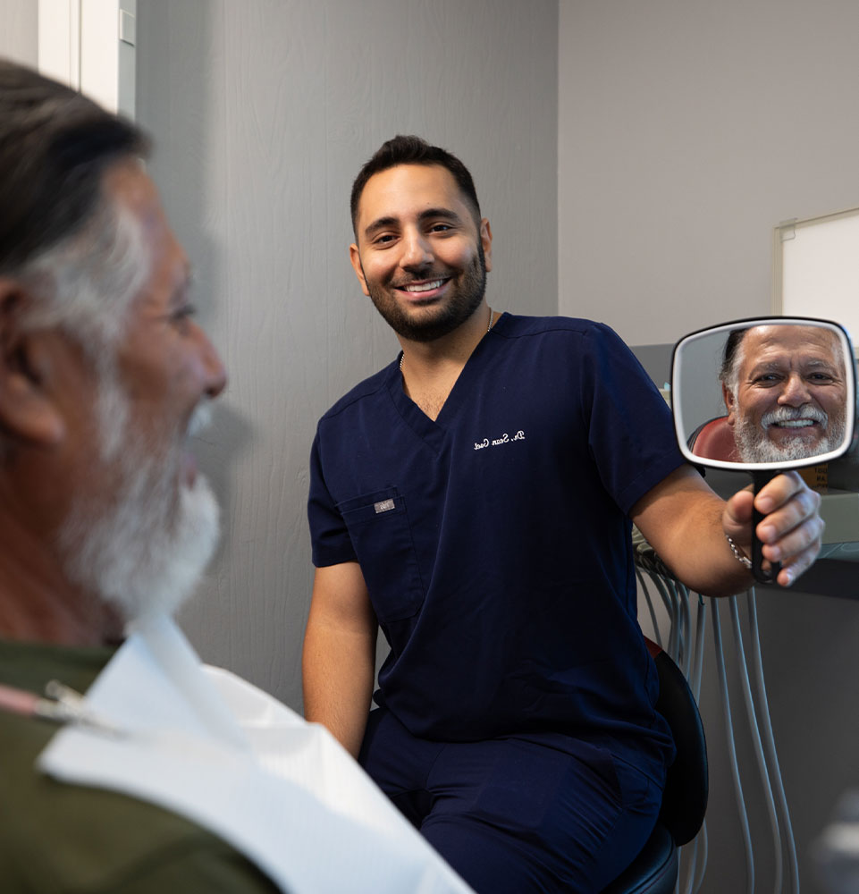 doctor showing up mirror to show patient teeth after procedure