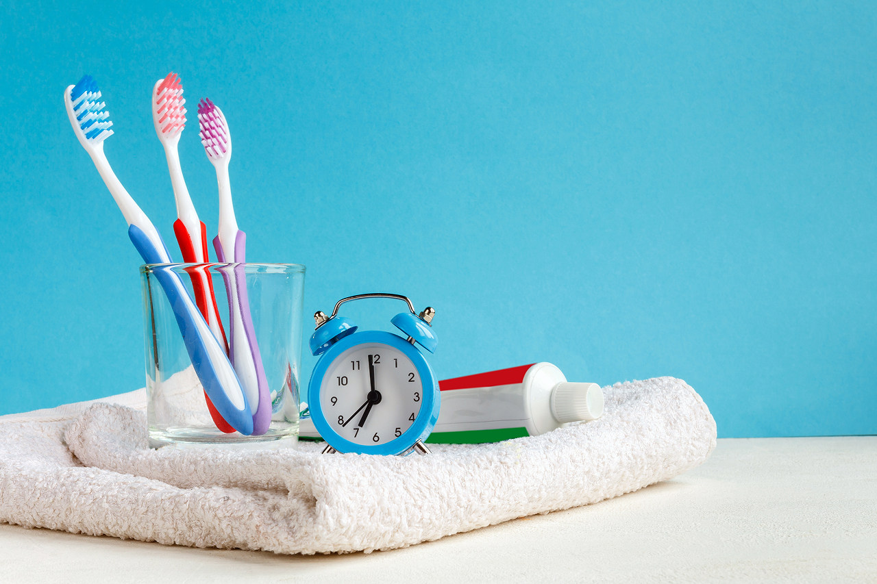 toothbrushes-clock-and-toothpaste-on-white-towel